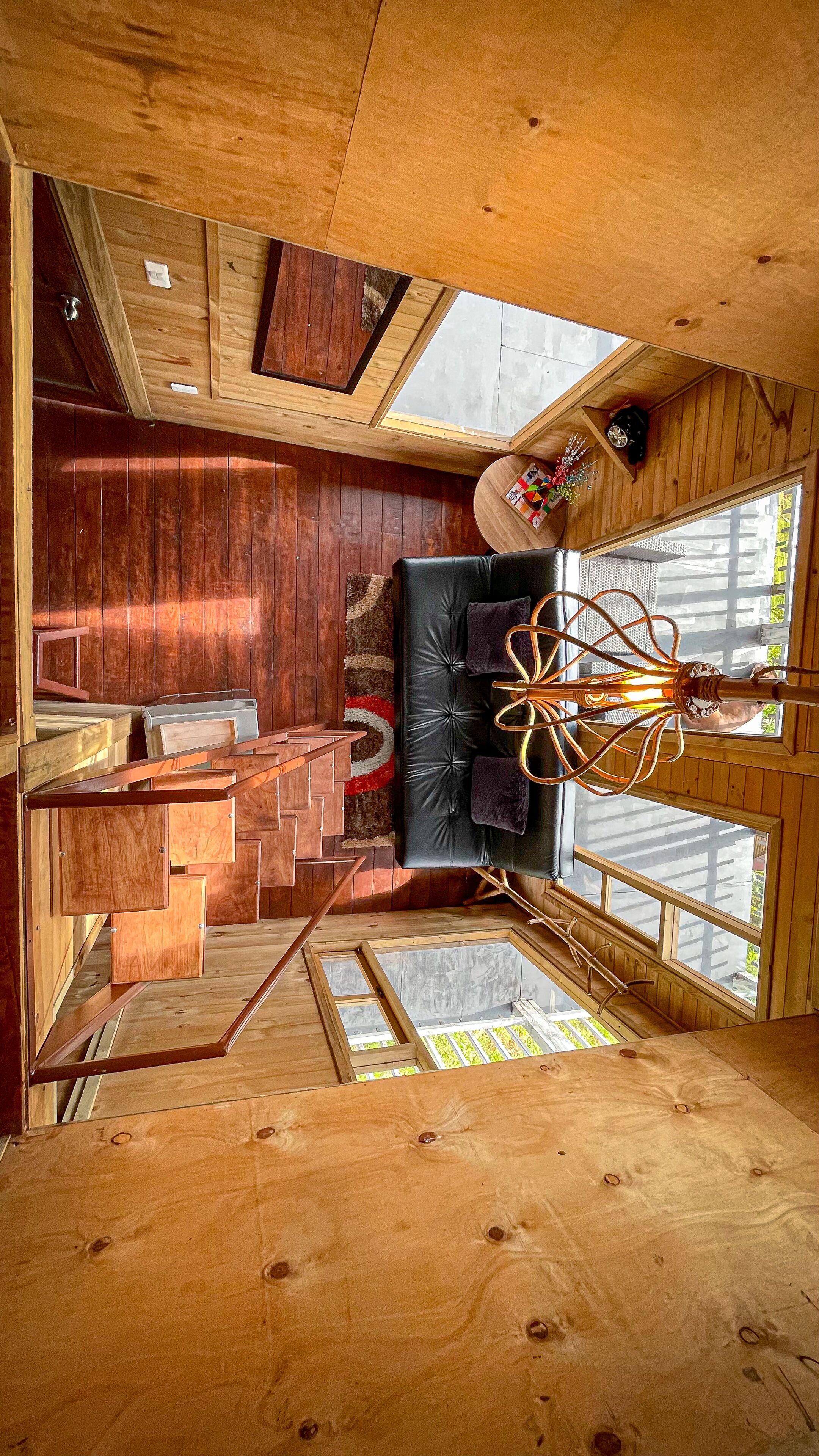 Un interior de cabaña moderno con suelo de madera, un sofá de cuero negro, una zona de comedor y una escalera que conduce a un nivel superior.