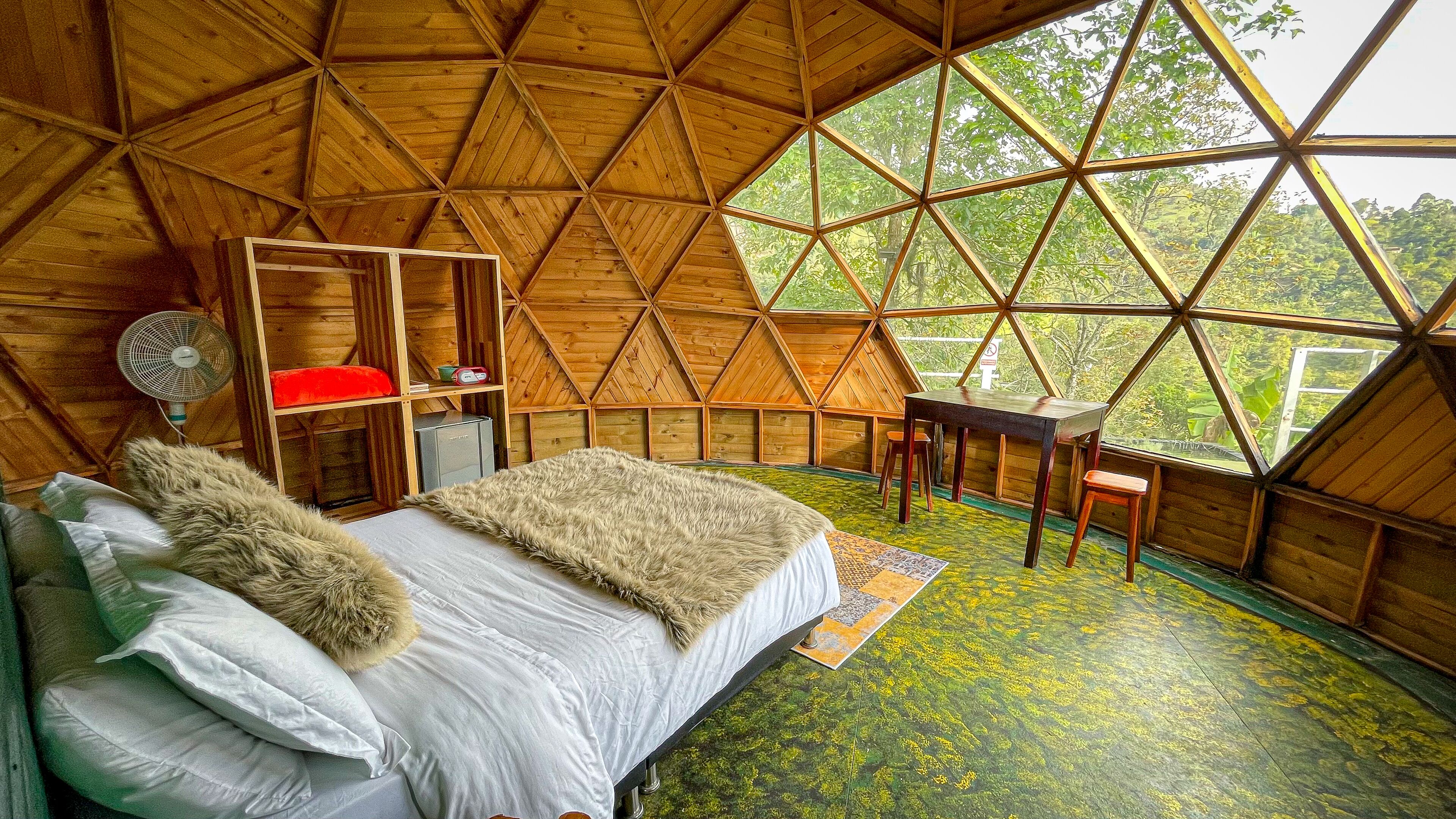 Una habitación acogedora con techo a dos aguas, una cama, una mesita y un ventilador.