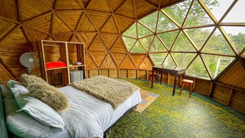 Una habitación acogedora con techo a dos aguas, una cama, una mesita y un ventilador.