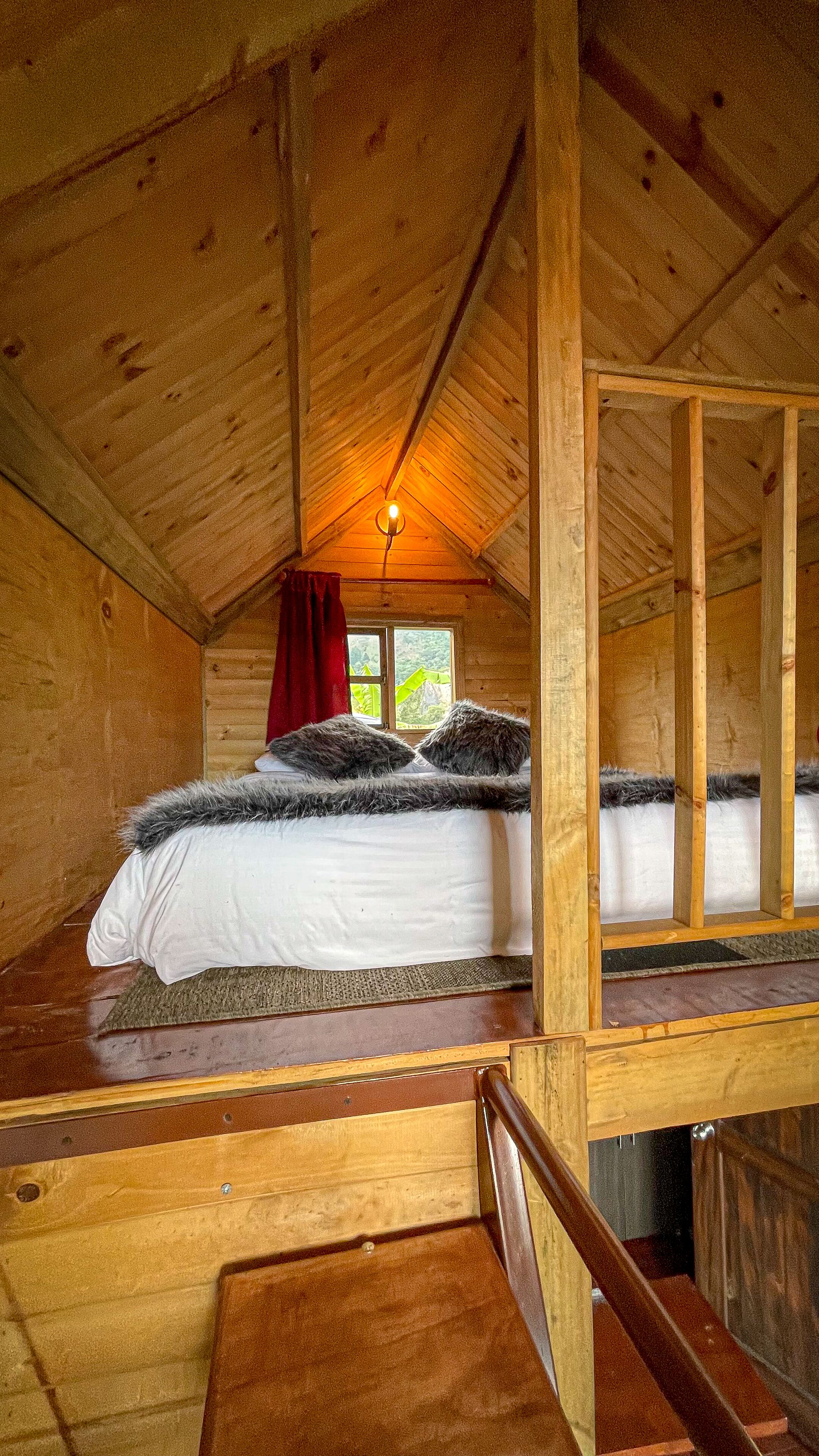 A wooden cabin bedroom with a bed, a window, and a red curtain.