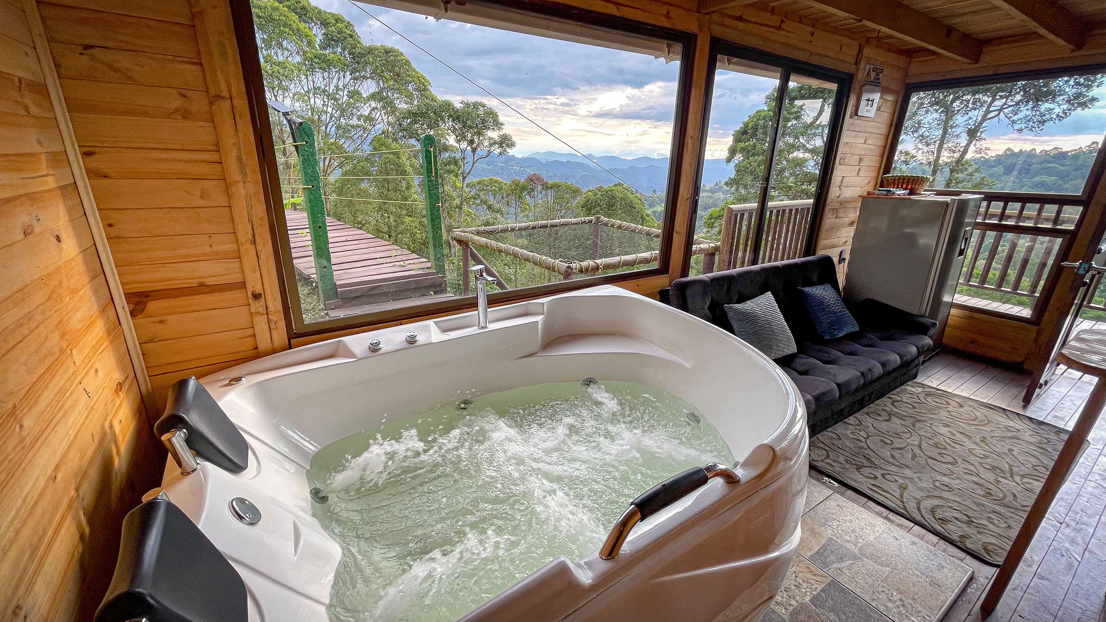 A wooden cabin with a hot tub, a sofa, and a view of mountains.