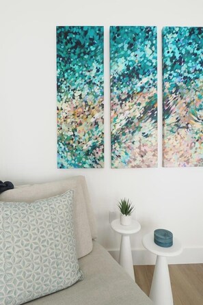 A room with a beige sofa, a patterned pillow, and a wall-mounted abstract painting.
