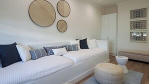 A modern living room with a white sofa, multiple pillows, a round ottoman, and wall art. - Oceanfront South Sound Home with Magical Sunsets! (Patricks Island)
