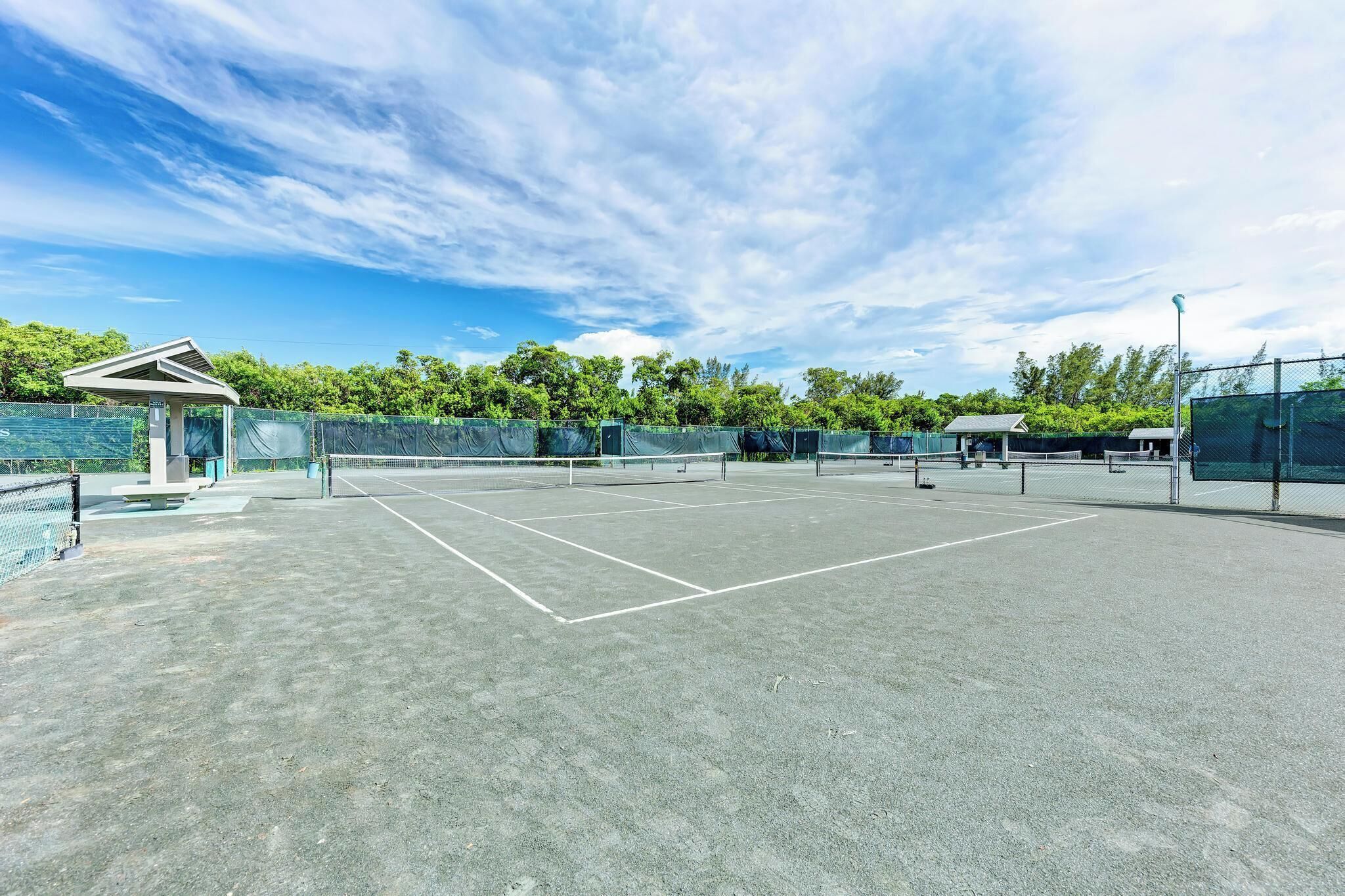 Una cancha de tenis al aire libre con un área de descanso cubierta y una valla.
