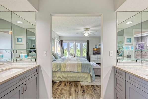 A bedroom with a large bed, a ceiling fan, and a view of the outdoors through a window.