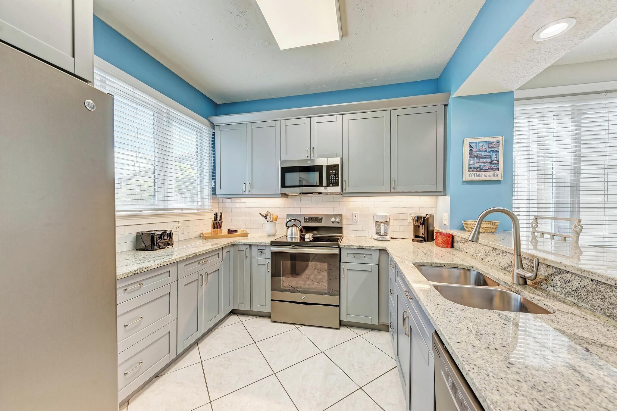 A modern kitchen with grey cabinets, stainless steel appliances, a double sink, and a microwave.