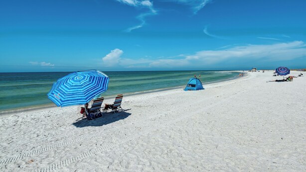 A beach with a tent, a striped umbrella, and beach chairs. - Longboat Key Cedars Beach House-pet Friendly-2 Minute To The Beach (Longboat Key)