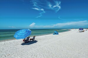 Uma praia com uma tenda, um guarda-sol listrado e cadeiras de praia.