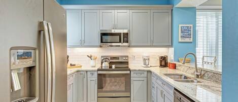 A modern kitchen with grey cabinets, a stainless steel refrigerator, a microwave, an oven, and a dishwasher.