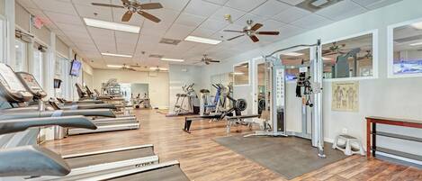 A gym with treadmills, exercise equipment, ceiling fans, and a wooden floor.