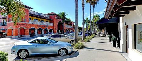 Una calle con coches estacionados, palmeras y edificios con rótulos como 'LMC Capital Advisors' y 'Norton’s Gourmet'.