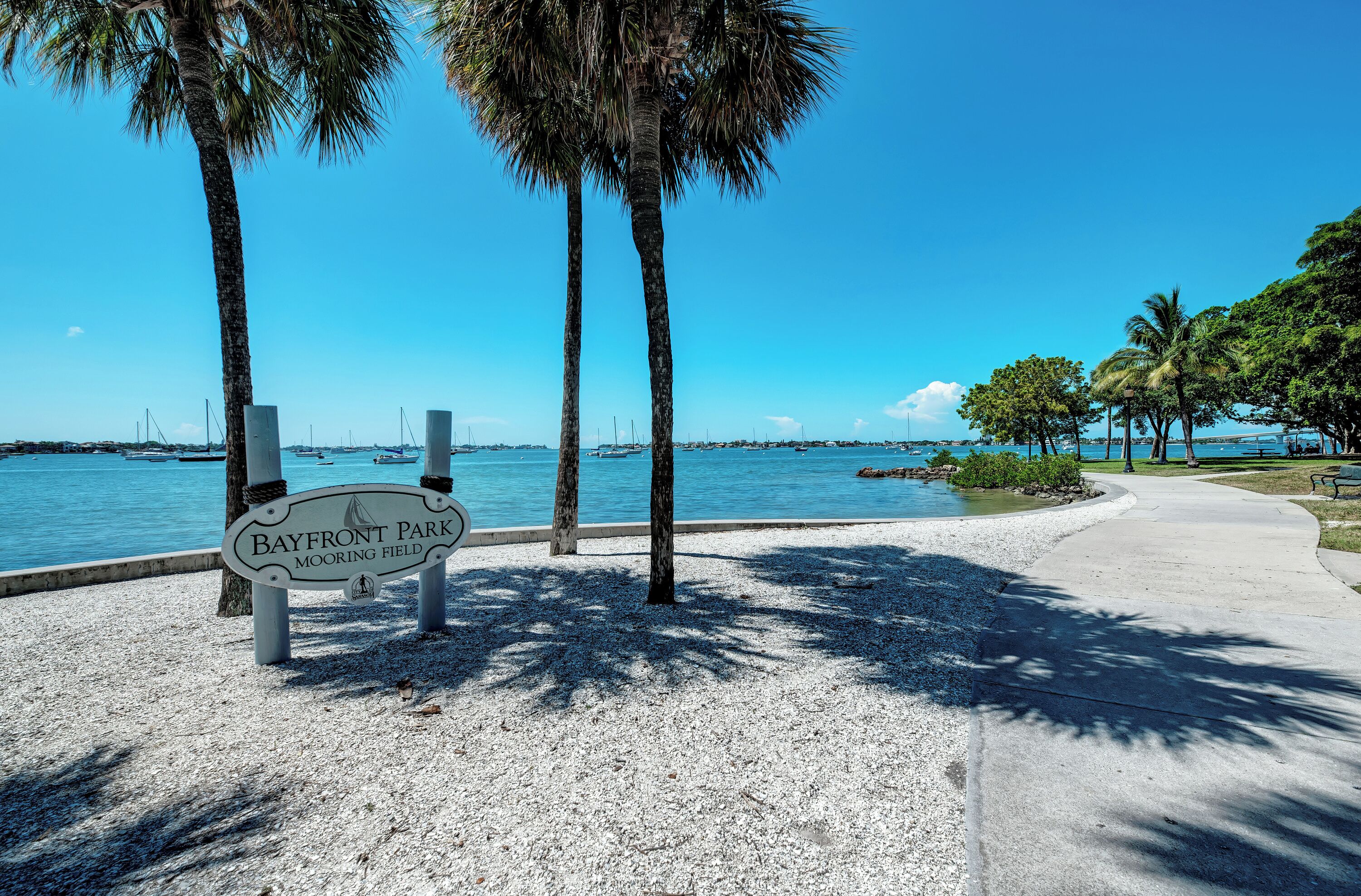 A park sign with a view of the water and boats in the background.
