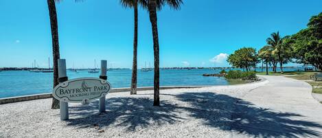A park sign with a view of the water and boats in the background.