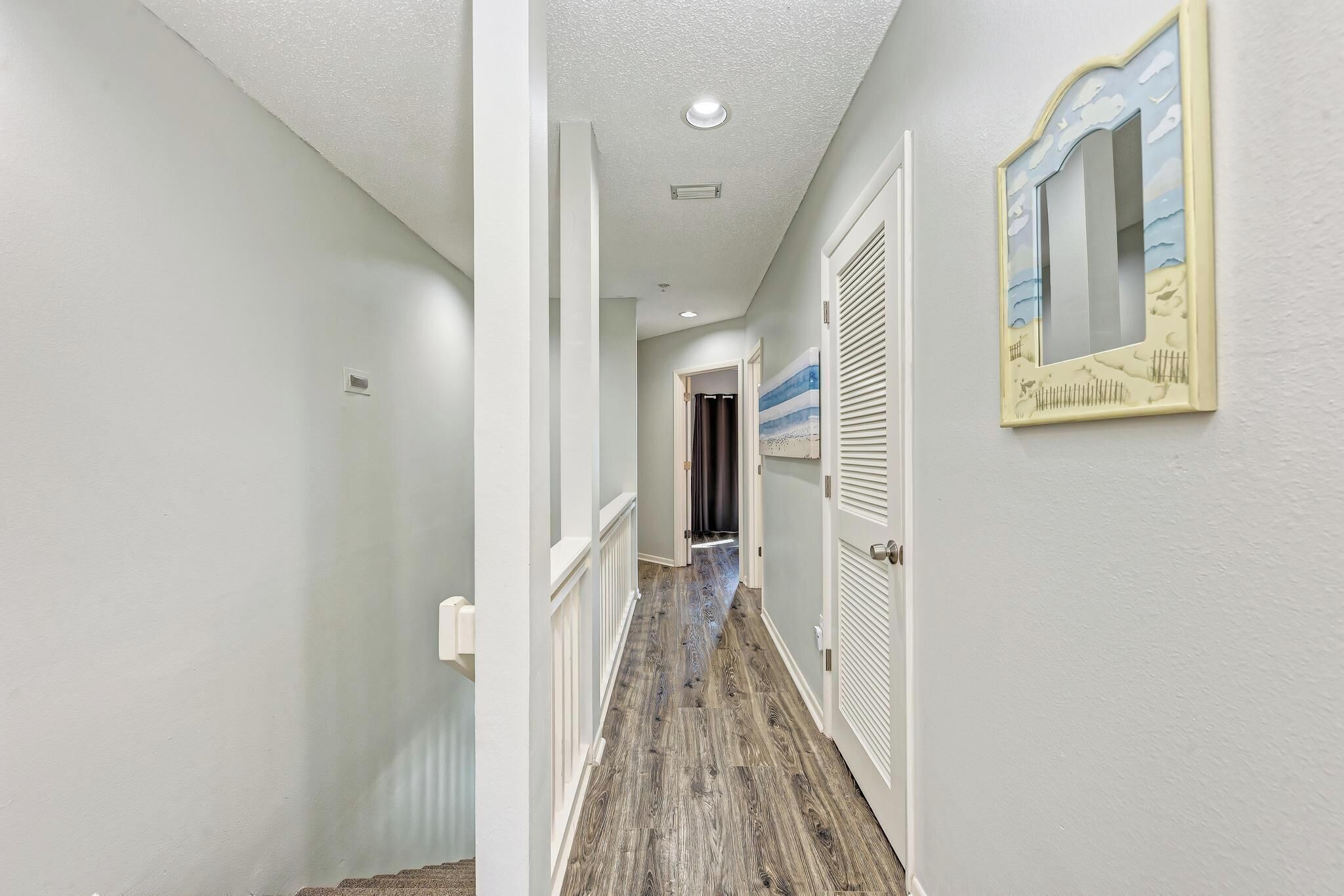 A hallway with a wooden floor, white walls, and a ceiling with recessed lighting.