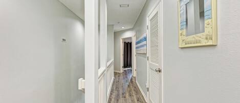 A hallway with a wooden floor, white walls, and a ceiling with recessed lighting.