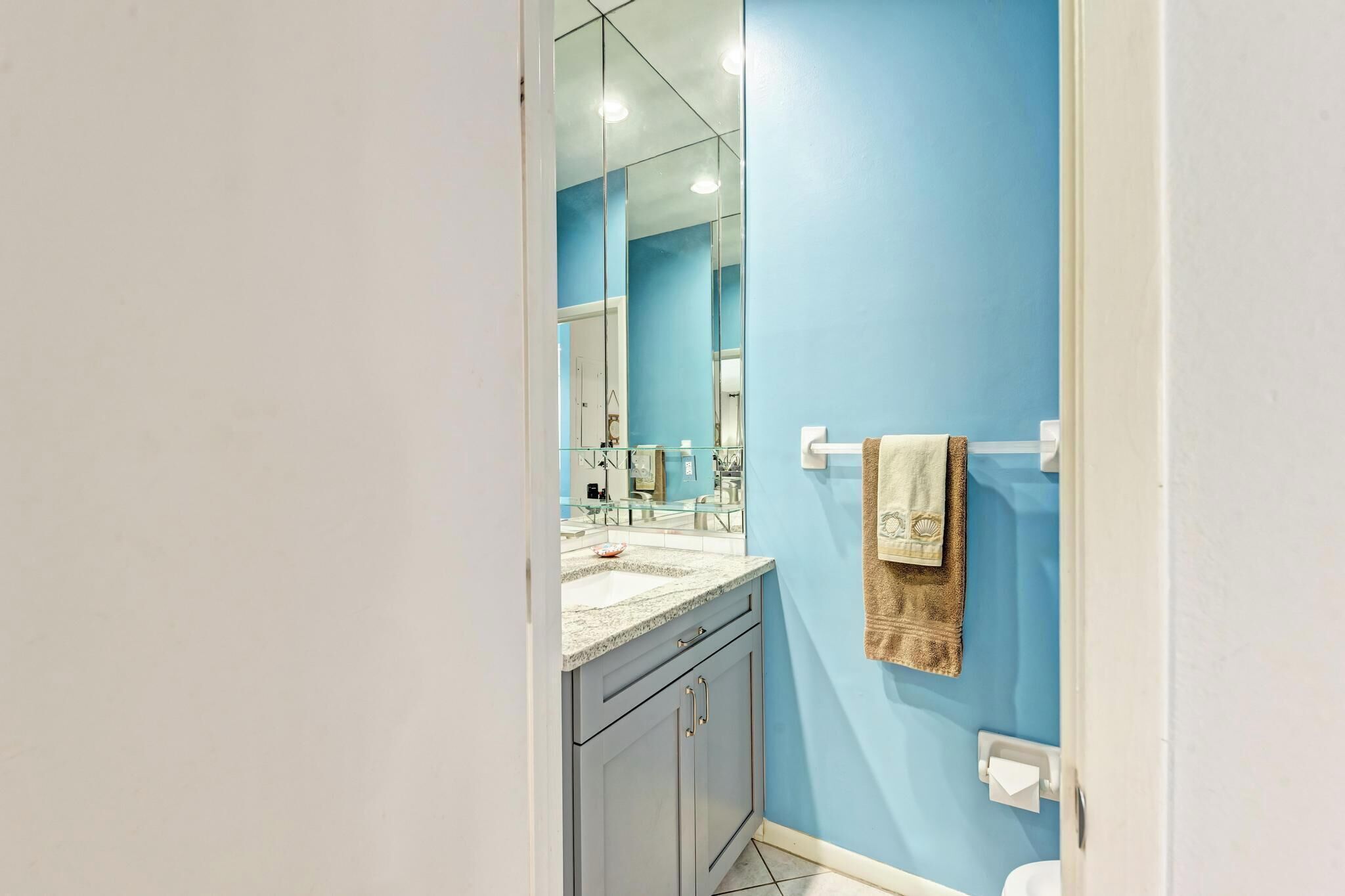 A bathroom with a blue wall, a sink with a mirror above it, and a towel hanging on the wall.