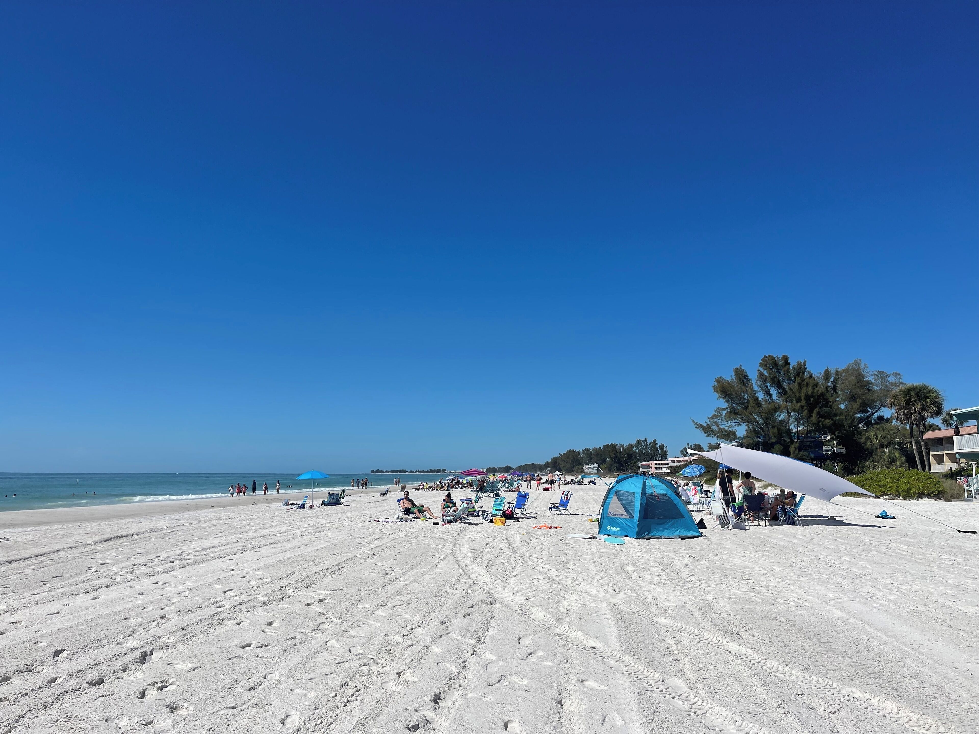 A sandy beach with a tent and umbrellas, clear skies, and a calm sea.