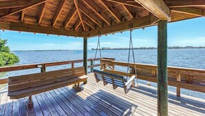 A wooden deck with benches and a swing, overlooking a body of water. - Bradenton Beach Club Bliss-2 Bedroom-2 Bathroom Condo-2 Pools-hottub-private Beach Access (Bradenton Beach)