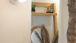 A narrow hallway with a wooden shelf holding a mirror, a vase with pampas grass, and a small potted plant. - Capella Skiathos Residences (Skiathos)