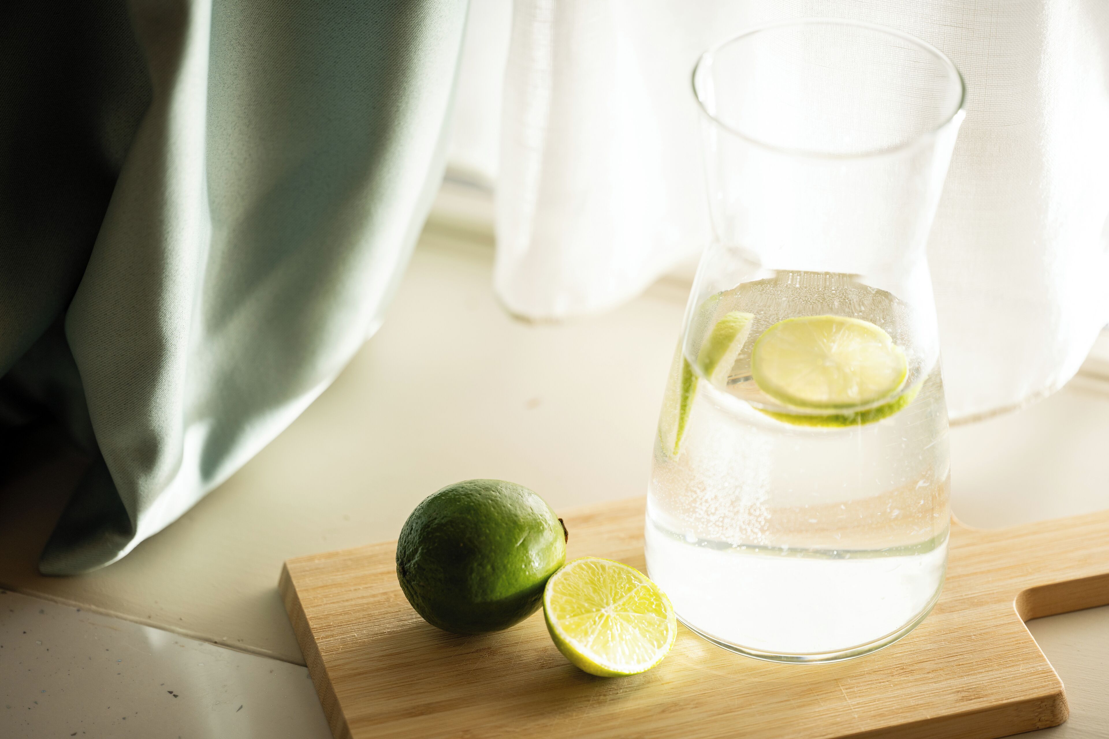 A glass of water with lime slices on a wooden board.