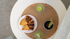 A round table with a plate of food, a drink, and a book on a patterned cushion. - Capella Skiathos Residences (Skiathos)