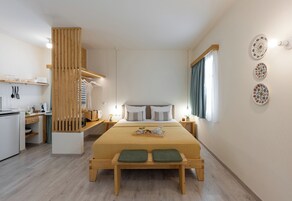 Habitación de hotel moderna con una cama de madera, una pequeña kitchenette, un área de comedor con un banco y vistas a la ciudad.