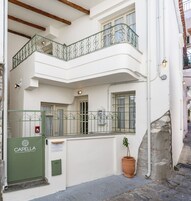 Un edificio de dos pisos con balcón, una puerta verde y una planta en maceta.