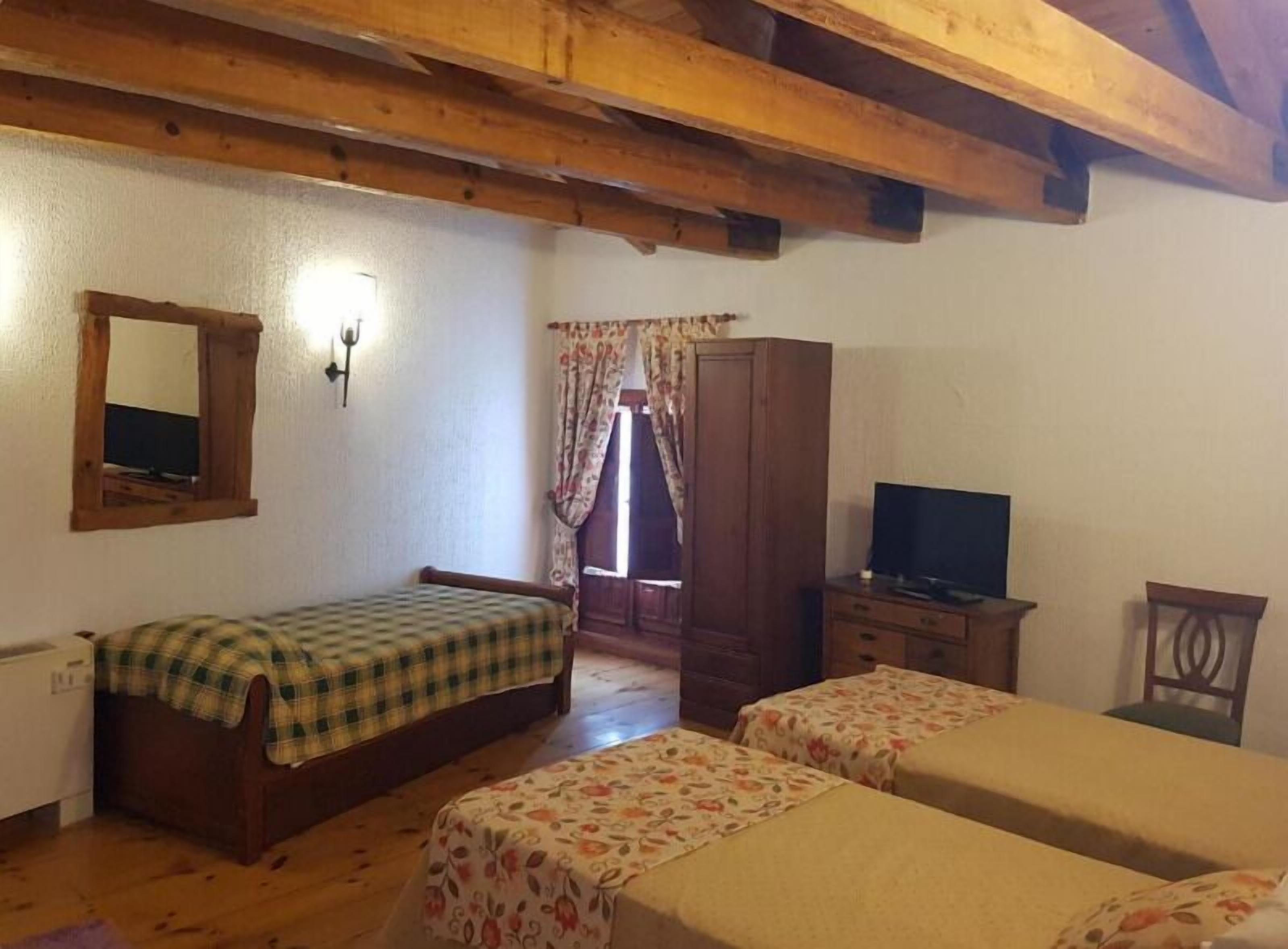 Una habitación con dos camas, un armario de madera, un televisor y un espejo en la pared.