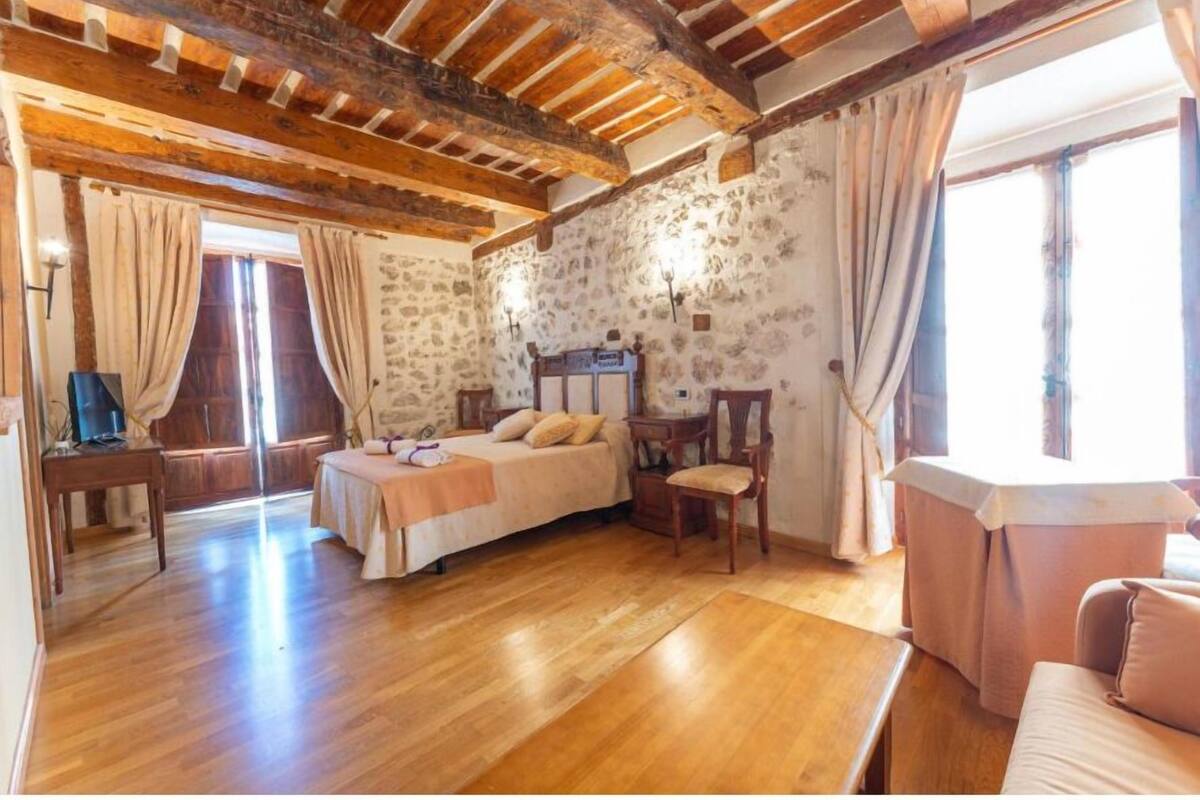 A room with a wooden ceiling, a bed, a chair, a table, and a sofa.