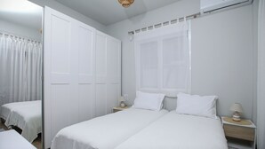 Habitación de hotel con dos camas, una mesita de noche con lámpara, aire acondicionado y un espejo.