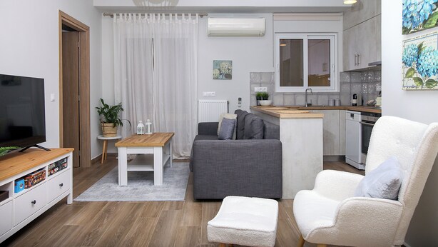 Una sala de estar moderna con un sofá gris, un sillón blanco, una mesa de centro de madera y un televisor de pantalla plana.