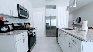 A modern kitchen with white cabinetry, a stainless steel refrigerator, a microwave, a stove, and a sink with a faucet. - 2024 New 3 Suites  5 min to Disney (Kissimmee)