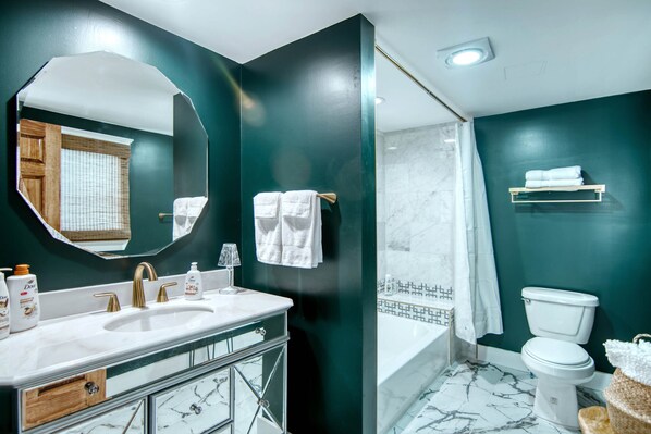 A modern bathroom with a large mirror, a sink with a gold faucet, a toilet, and a shower area.