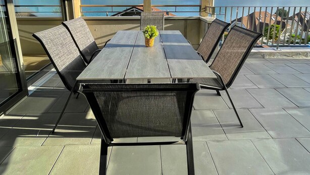 A dining area with a table and chairs, large windows with a mountain view, and a balcony railing. - Chez Marie See I Berge I Luzern (Beckenried)