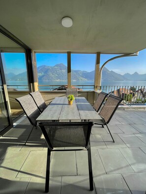 Uma área de refeições com mesa e cadeiras, janelas amplas com vista para as montanhas e um parapeito de varanda.