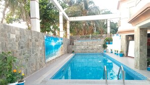 A swimming pool with a stone wall and a mural, surrounded by potted plants and a covered area. - Hotel Suite Sadaf (Cox's Bazar)