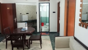 A hotel room with a dining area, a sofa, a kitchen with a refrigerator, and a bathroom visible through an open door. - Hotel Suite Sadaf (Cox's Bazar)