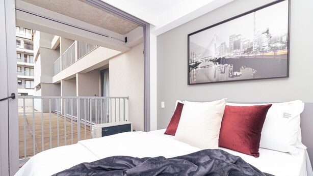A hotel room with a bed, a cityscape painting, and a view of an outdoor balcony with a railing. - Vossa Bossa Moema ON (São Paulo)