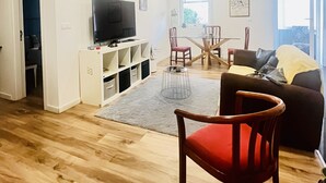 Una sala de estar moderna con un televisor de pantalla plana, un comedor con una mesa y sillas de madera, y una silla roja en primer plano.