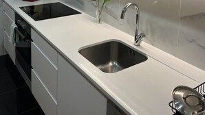 Una cocina moderna con armarios blancos, un lavamanos de acero inoxidable y un horno empotrado.