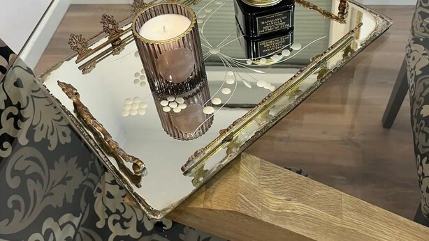 Una mesa de centro de cristal con una bandeja decorativa, una vela y un recipiente de vainilla de Madagascar.