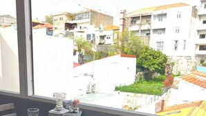 Un balcón con una mesa, sillas, una botella de licor y dos vasos. Se ve un jardín y edificios en la distancia.