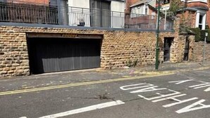 A street with a stone wall and a closed garage door. - Lovely two bed flat with free parking (Nottingham)