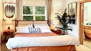 Una camera da letto con un letto grande, due comodini, un tavolino, una pianta in vaso e una finestra con tende.