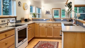 Una cucina moderna con mobili in legno, forno integrato, una grande isola con lavello e vista sull'esterno attraverso ampie finestre.