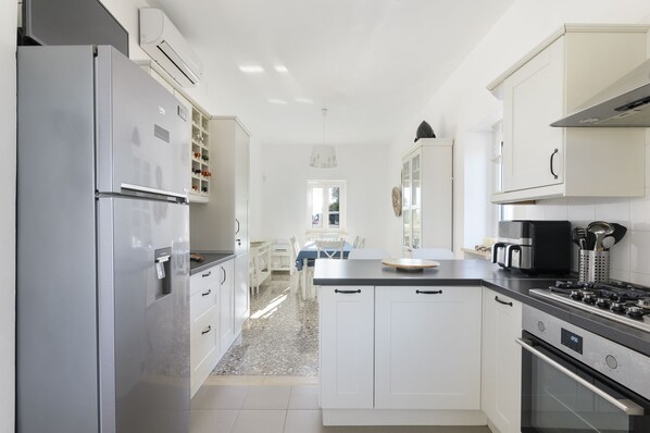 A modern kitchen with white cabinetry, a stainless steel refrigerator, a gas stove, and a dining area with a table and chairs. - Villa Gabriella con piscina by Wonderful Italy (Ostuni)
