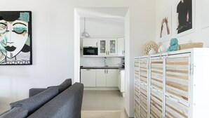 Moderni keittiö, jossa on valkoiset kaapit, mikroaaltouuni ja pesuallas. Etualalla on harmaa sohva ja koristeellinen seinäelementti.