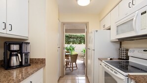 Cocina compacta con cafetera, microondas y estufa. Un acceso da a un patio con mesa y sillas.