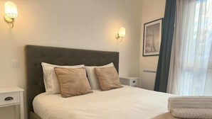 A neatly made bed with a grey headboard, two bedside tables, and a framed picture on the wall. - Charming apartment with terrace, near Paris (Courbevoie)