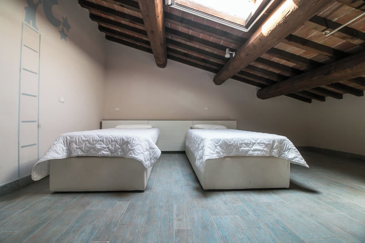 Un dormitorio pequeño estilo altillo con dos camas individuales, un tragaluz y vigas de madera a la vista.